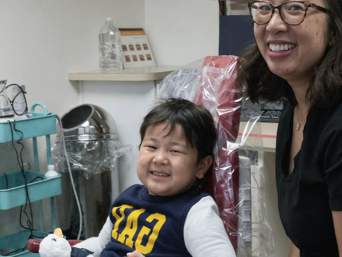Dr. Tam Nguyen beside a smiling child in a treatment room at Mason Park Dental for Kids