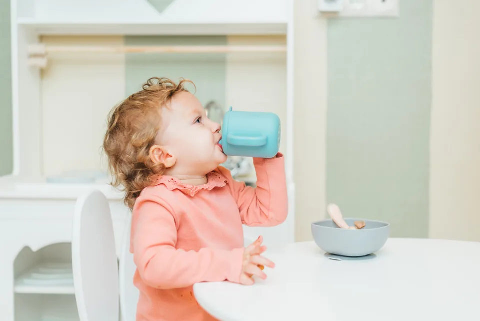A toddler drinking from a cup in a high chair