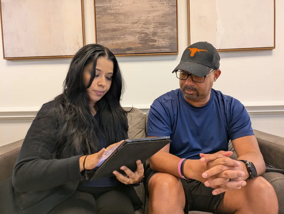 Two parents on the waiting-room sofa with the check-in tablet