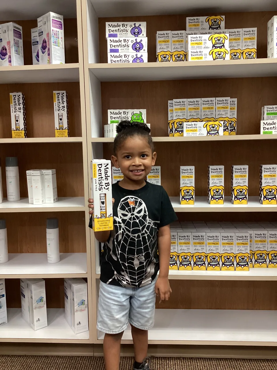 A smiling boy holding a toothpaste box at the product shelf by the front desk