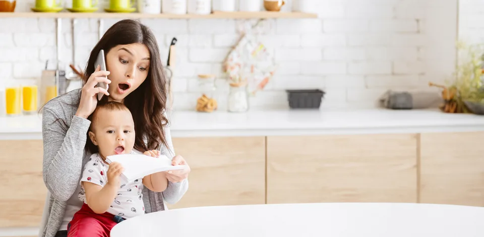 A parent on the phone at the kitchen table, a child on her lap