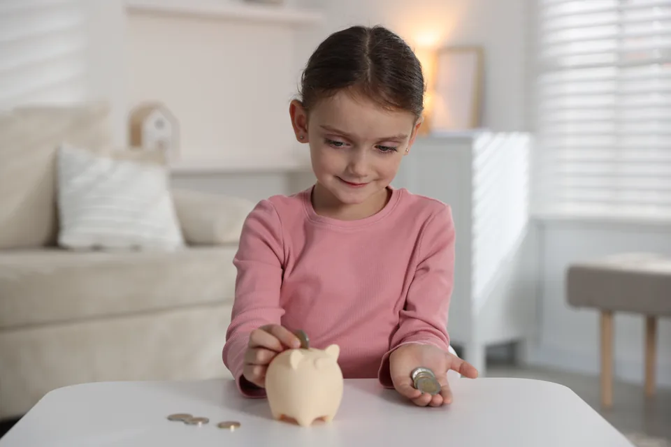 A girl dropping a coin into a piggy bank