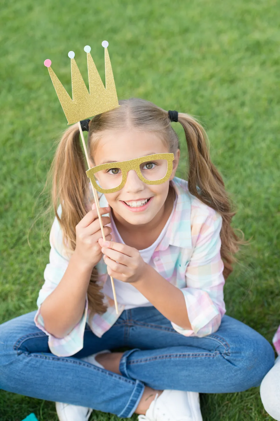 A girl in a paper crown, sitting on the grass